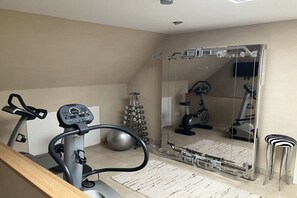 Une salle de sport à domicile équipée de matériel d’exercice, dotée d’un grand miroir et d’un plancher en bois.