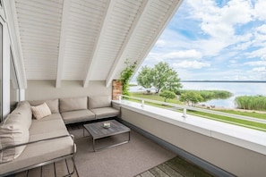 A balcony with a sofa and a table, overlooking a body of water and greenery. - Holiday apartment with 1 bedroom (Rankwitz)
