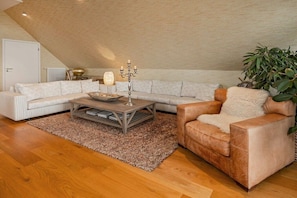 A modern living room with a sloped ceiling, a sectional sofa, a leather armchair, a wooden coffee table, and a decorative candelabra. - Holiday apartment with 1 bedroom (Rankwitz)