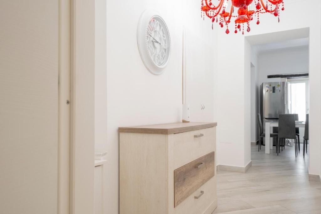 A hallway with a wooden cabinet, a wall clock, and a red chandelier.