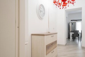 A hallway with a wooden cabinet, a wall clock, and a red chandelier. - Ortigia Inner Suites (Siracusa)
