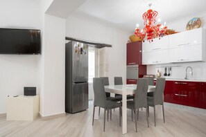 A modern kitchen with a dining area, a TV, and a red chandelier. - Ortigia Inner Suites (Siracusa)