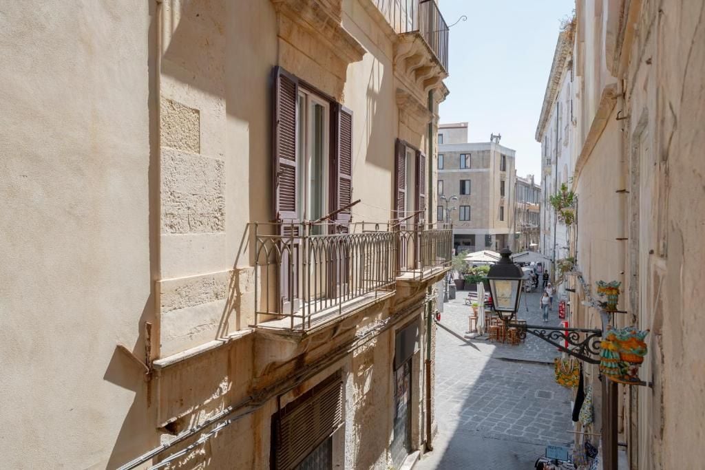 Una calle estrecha flanqueada por edificios, con balcones que tienen barandillas metálicas y contraventanas.