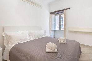 A hotel room with a bed, a nightstand, a window, and a door. - Ortigia Inner Suites (Siracusa)