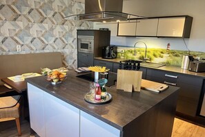 A modern kitchen with a central island, built-in appliances, and a view of a coastal landscape. - Wadden Sea walkers - calm winds (Wurster Nordseeküste)