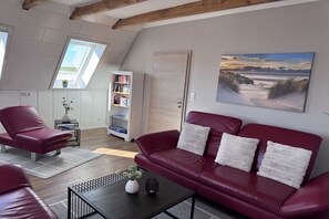 A living room with a red leather sofa, a coffee table, and a bookshelf. - Wadden Sea walkers - calm winds (Wurster Nordseeküste)