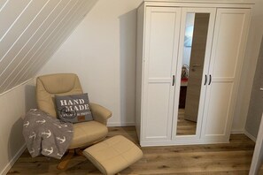 A room with a white wardrobe, a beige armchair, and a matching ottoman. - Wadden Sea walkers - calm winds (Wurster Nordseeküste)