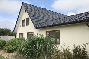 Une maison de plain-pied avec un toit en pente, une façade blanche et un petit jardin agrémenté de différentes plantes.