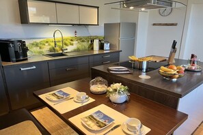 Cozinha moderna com área de jantar, equipada com cafeteira, torradeira e uma tigela de frutas.