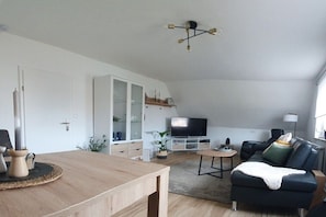 Un soggiorno moderno con un tavolo da pranzo in legno, un divano nero, una televisione e una lampada a sospensione.