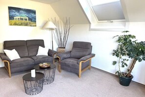 Een woonkamer met een bank, fauteuil, salontafel, lamp en een potplant.
