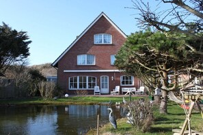 A two-story brick house with a pond in the front yard, surrounded by trees and a wooden fence. - Holiday home Johren Apt. 1 (Norderney)
