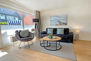 Een moderne woonkamer met een bank, fauteuil, salontafel en kunst aan de wand.