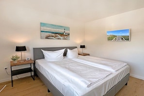 A bedroom with a bed, two bedside tables with lamps, and two wall-mounted paintings. - Holiday apartment with 1 bedroom (Westerland)