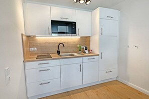 A compact kitchen with white cabinets, a black microwave, and a wooden countertop. - Holiday apartment with 1 bedroom (Westerland)