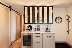 A compact kitchen with a built-in coffee maker, a clock, and a cabinet with glass doors. - Ski-In/Out Condo, Hot Tub & Rooftop Fire Pit (Park City)