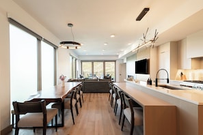 A modern kitchen with a long island, dining area, and large windows. - Ski-In/Out Condo, Hot Tub & Rooftop Fire Pit (Park City)