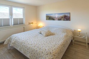 A bedroom with a large bed, two bedside lamps, a window with blinds, and a painting on the wall. - House by the Lighthouse - Holiday Apartments (Neuharlingersiel)