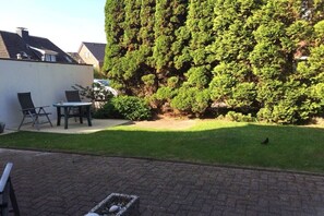A patio area with a table and chairs, a hedge, and a lawn. - House by the Lighthouse - Holiday Apartments (Neuharlingersiel)