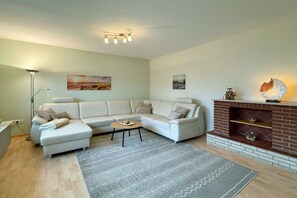 A modern living room with a sectional sofa, a coffee table, a fireplace, and artwork on the walls. - House by the Lighthouse - Holiday Apartments (Neuharlingersiel)