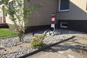 En bygning med murstensfacade, et lille haveareal med et træ, en klippehave og en rødhvid struktur, der ligner et fyrtårn.