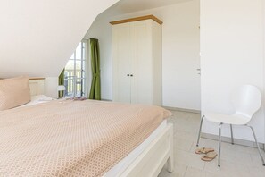 A bedroom with a bed, a chair, a wardrobe, and a window with curtains. - Black-headed gull with a view of the Baltic Sea (Zierow)