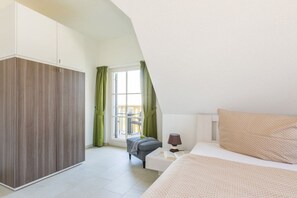 A bedroom with a bed, a nightstand, a lamp, a window with curtains, and a wardrobe. - Black-headed gull with a view of the Baltic Sea (Zierow)