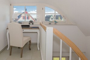 Una habitació amb escriptori, cadira i vista cap a cases a través d'una finestra.
