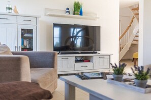A living room with a flat-screen TV on a white cabinet, a sofa, a coffee table, and a staircase in the background. - Black-headed gull with a view of the Baltic Sea (Zierow)
