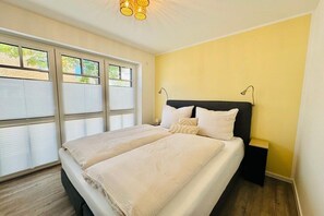 Ein Doppelbett mit Kopfteil, Nachttischlampen und einem Fenster mit Jalousien.
