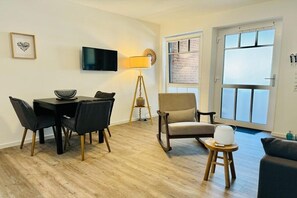 Ein modernes Wohnzimmer mit Esstisch, Stühlen, einer Couch, einem Fernseher, einer Lampe und einem Fenster mit Blick.