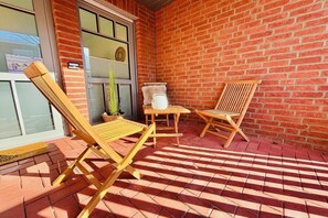 Um pátio com paredes de tijolo, duas poltronas de madeira e uma pequena mesa.