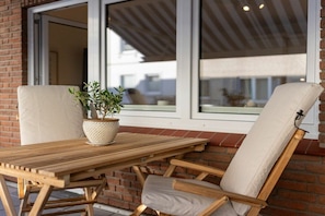 A wooden table and two chairs with cushions, positioned near a window with a view of buildings. - Holiday apartment with 1 bedroom (Norderney)