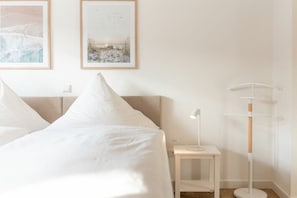Un dormitorio con una cama, una mesita de noche con lámpara y dos cuadros en la pared.