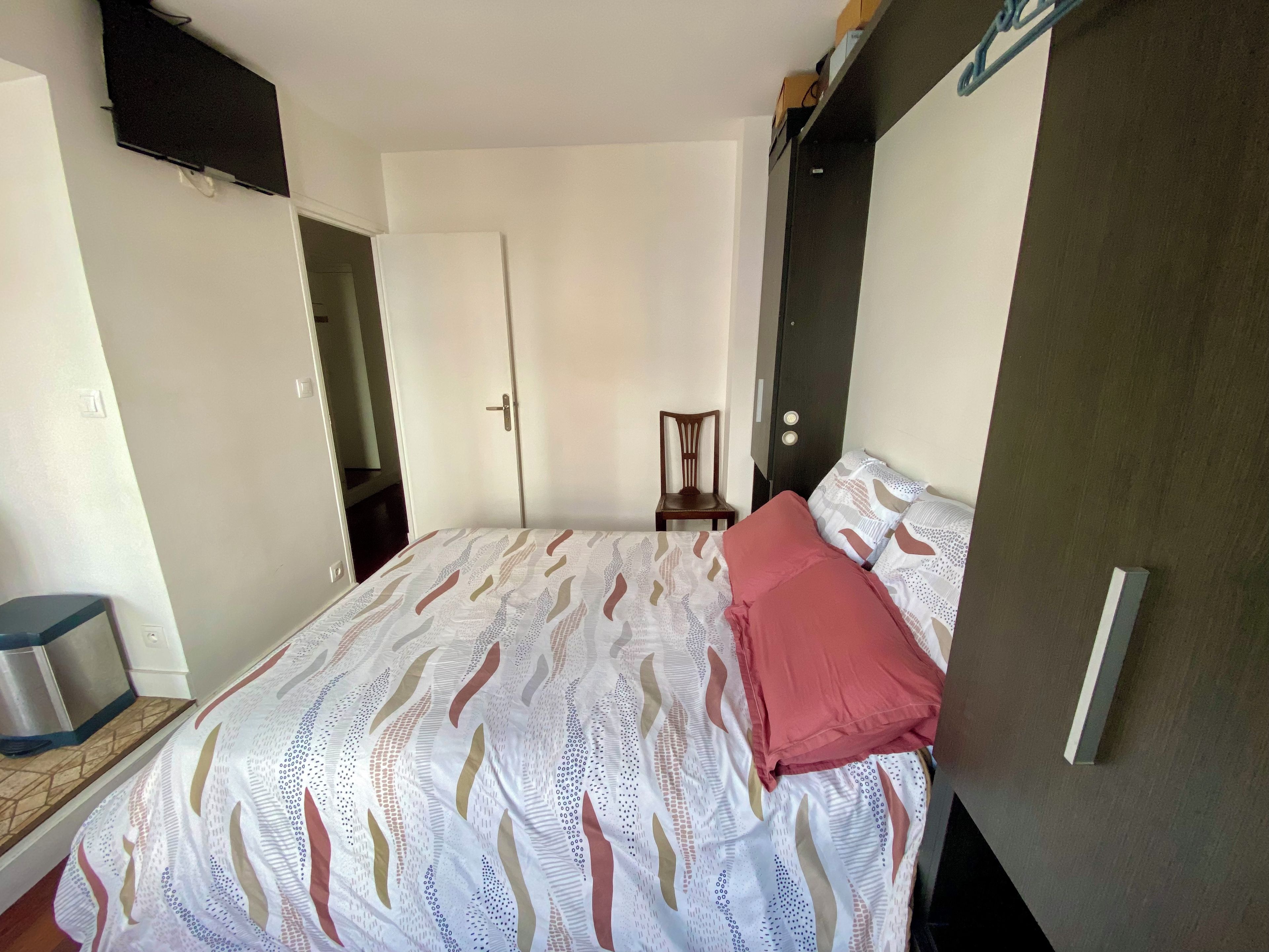 Un dormitorio con cama, una silla, armario y puerta.