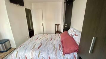 Un dormitorio con cama, una silla, armario y puerta.