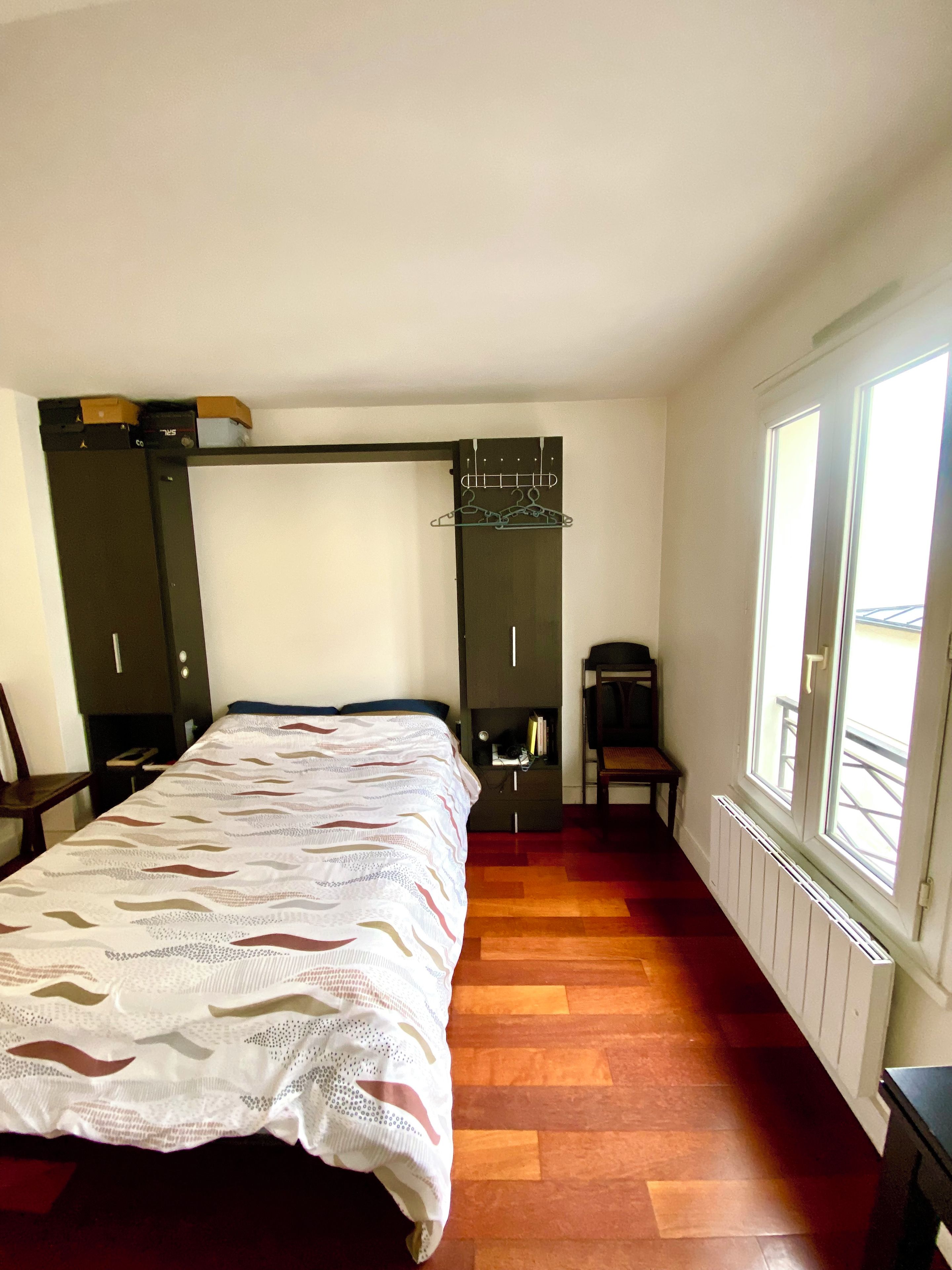 Une chambre à coucher avec un lit, une chaise, un porte-manteau et une fenêtre.