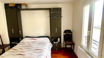 Une chambre à coucher avec un lit, une chaise, un porte-manteau et une fenêtre.