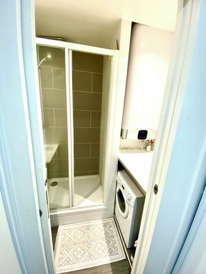 Une petite salle de bain comprenant une douche, des toilettes et un lave-linge.