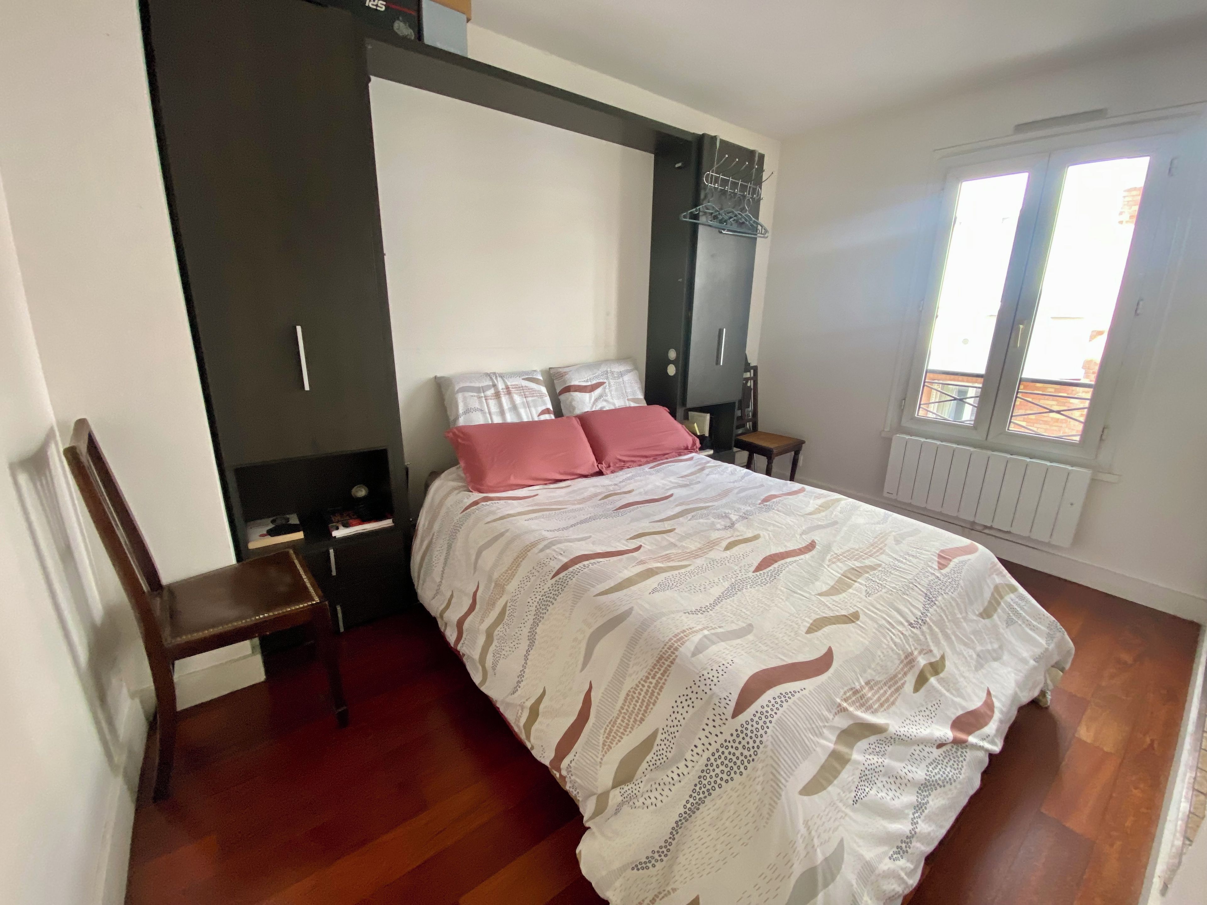 Een slaapkamer met een bed, een stoel, een kledingkast, een radiator en een raam.
