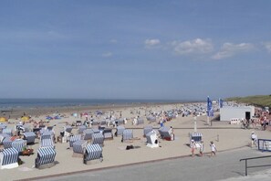 A beach with numerous striped beach chairs and umbrellas, a sandy walkway, and a clear view of the ocean. - Holiday apartment with 1 bedroom (Norderney)