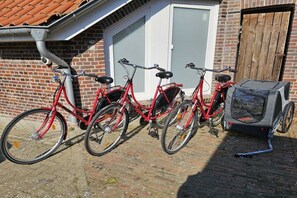 A row of red bicycles parked outside a brick building with a white door and a wooden gate. - Holiday home in Dunum with sauna (Dunum)