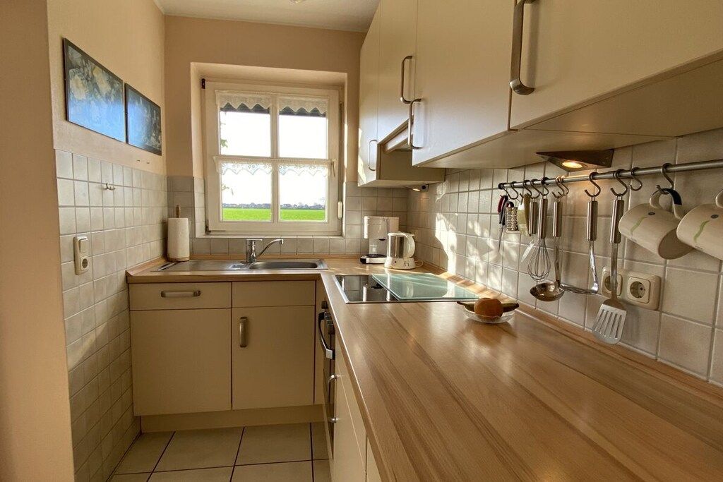 A kitchen with a window, a sink, cabinets, and various utensils hanging on the wall.