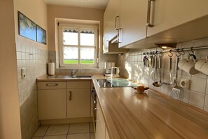 A kitchen with a window, a sink, cabinets, and various utensils hanging on the wall. - Holiday home with 3 bedrooms (Carolinensiel)