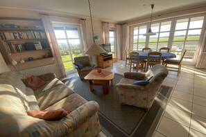 A living room with a sofa, armchairs, a coffee table, a TV, and a dining table with chairs. - Holiday home with 3 bedrooms (Carolinensiel)