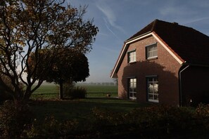 A brick house with a sloped roof, two windows, and a view of a green field. - Holiday home with 3 bedrooms (Carolinensiel)