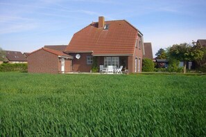 A two-story house with a red-tiled roof and a brick exterior, surrounded by a green field. - Holiday home with 3 bedrooms (Carolinensiel)