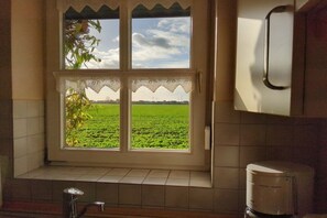 A kitchen with a window overlooking a green field, a sink, and a white appliance. - Holiday home with 3 bedrooms (Carolinensiel)
