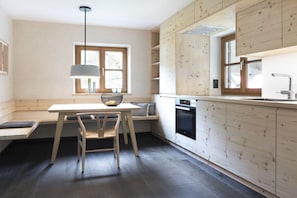 A modern kitchen with wooden cabinetry, a built-in oven, and a dining area with a bench and table. - Landhaus Bader, holiday apartment Waxenstein (Grainau)