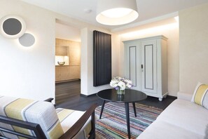 A modern hotel room with a sofa, a round table with flowers, a cabinet, and a wall-mounted light fixture. - Landhaus Bader, holiday apartment Waxenstein (Grainau)